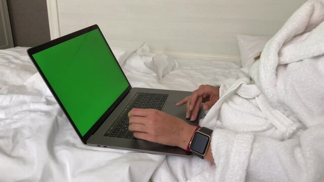 MOSCOW CITY, RUSSIA - AUGUST 10,2020: Woman working on macbook while lying in bed in hotel in a bathrobe