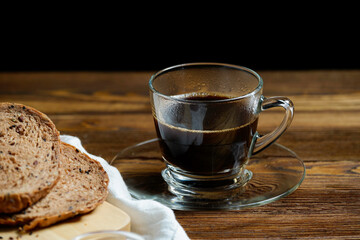 Hot black coffee, americano in glass cup with multi grain chocolate bread on wooden table with black background. Close up.