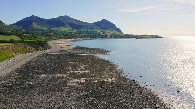Drone flying over Trefor Beach and rugged Welsh coast in Wales with Yr Eifl Mountains in background on sunny day