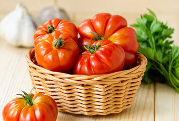 Ripe red tomatoes in basket on light wooden background