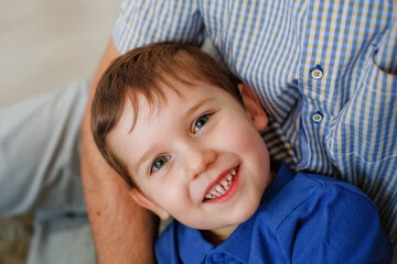 Portrait of a charming little boy, smiling, lying in the arms of a parent. Cute happy laughing boy. A handsome boy with a toothy smile looks at the camera.