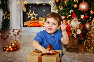 Fototapeta na wymiar Cute boy at the Christmas tree and fireplace, decorated with garlands and gifts. New year mood