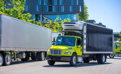 Medium-sized rig semi truck with box trailer turns on the city street towards a warehouse
