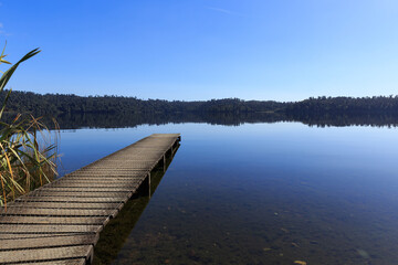Fototapeta premium Wooden pier in the morning at calm mirror lake with mountain background in New Zealand.