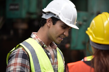 Portrait of young handsome technician man or industrial worker with hard hat or helmet and vest jacket working electronic machinery and mechanical engineering in Factory of manufacturing place