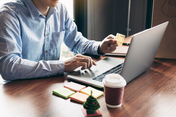 Young asian man typing laptop keyboard and holding credit card at home with online shopping or internet banking concept.