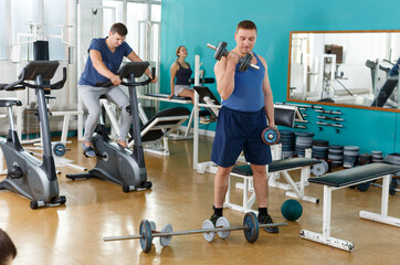 Fototapeta na wymiar Positive young man doing exercises with sports dumbbells at gym