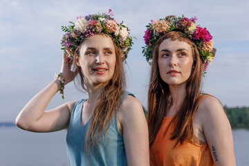 Two young and lovely girls in flower wreaths in nature. Ancient pagan origin celebration concept. Summer solstice day. Mid summer. Ancient rituals.
