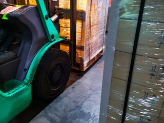 Naklejka premium Worker driving forklift loading shipment carton boxes goods on wooden pallet at loading dock from container truck to warehouse cargo storage in freight logistics, transportation industrial, delivery