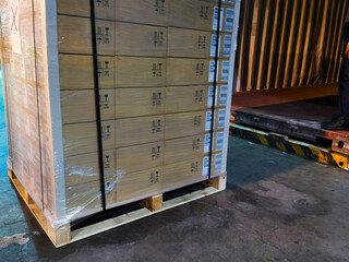 Worker driving forklift loading shipment carton boxes goods on wooden pallet at loading dock from container truck to warehouse cargo storage in freight logistics, transportation industrial, delivery