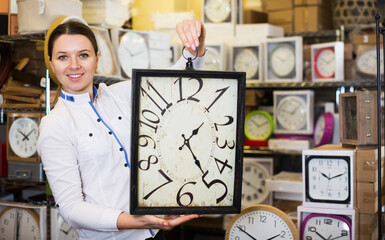 Young happy woman is holding clock in the furniture store.