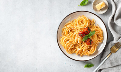 Italian spaghetti with cherry tomatoes in a white plate on a light background, top view, copy space
