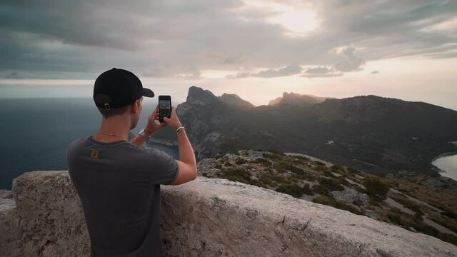 A young man arriving to a viewpoint on a watchtower and taking a photo of the landscape with his smartphone