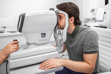 Handsome man checking eyesight in a clinic using diagnostic ophthalmic equipment. Patient checking...