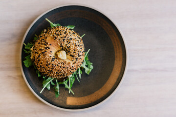 Bagel with sesame seeds, hummus and vegetables on black plate. View from above.