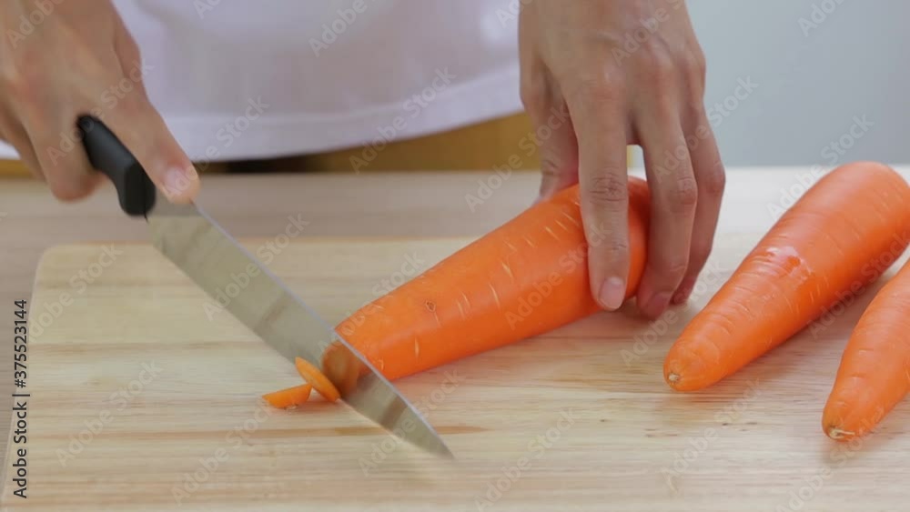 Wall mural woman is slicing fresh carrot on wooden cutting board