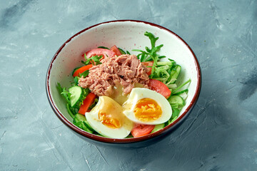 Healthy salad with canned tuna, egg and hollandaise sauce in a white bowl on a gray background
