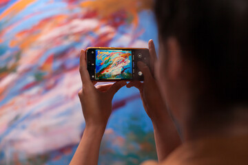 Young artist taking photo of masterpiece painting in art workshop. Modern artwork paint on canvas,...