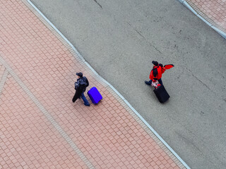 Men with suitcases on wheels walk along the road in the street. View from above