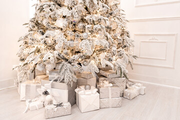 Christmas presents under New Year tree with artificial snow with golden illumination. Silver color