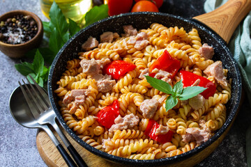 Healthy lunch. Fusilli pasta with canned tuna, grilled red peppers and tomatoes in frying pan on a stone countertop.