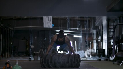 Maximum power! Pushing your limits. A powerful diverse athlete using his strength. Moving a tire in gym. Shot in 4k.  