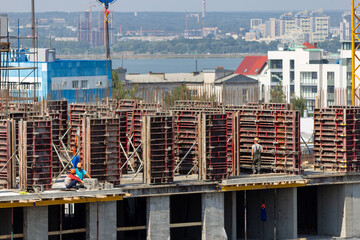 People are working on the construction site with cityscape on the background. Active urban development and summer constructions