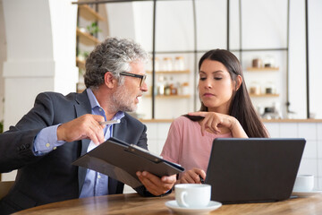 Serious mature legal expert reading, analyzing and explaining document to female customer. Man and woman sitting at table and discussing papers. Expertise and paperwork concept