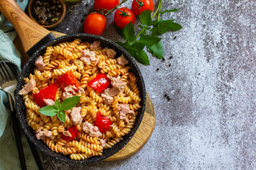 Healthy lunch. Fusilli pasta with canned tuna, grilled red peppers and tomatoes in frying pan on a stone countertop. Top view flat lay background. Copy space.