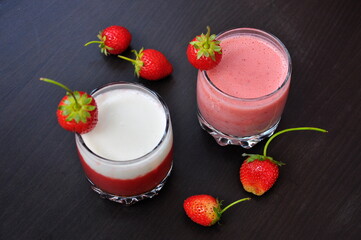 Two glasses of healthy smoothies with strawberry on the black table.