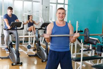 Fototapeta na wymiar Young man in sportswear doing exercises with barbell in gym