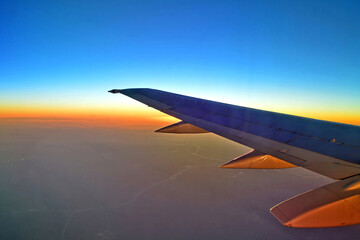 Blurred view of aircraft wing silhouette with  blue sky horizon and earth background in sun set time, viewed from airplane window
