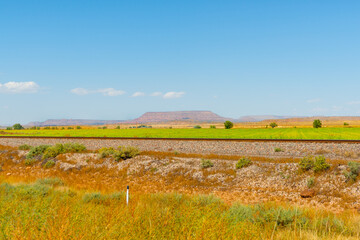Fototapeta premium Flat plains of New Mexico with distant flat-top mesa landform in distance and railway tracks through foreground.