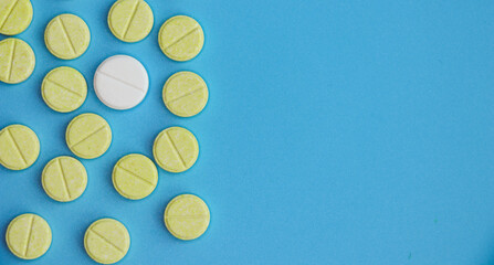 Round yellow tablets are scattered on a blue background, and one tablet is white. Free space for copying.
