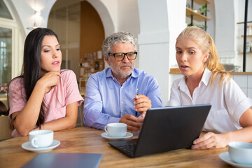 Confident female manager showing presentation on laptop to young woman and mature man, speaking and explaining details. Consulting or communication concept