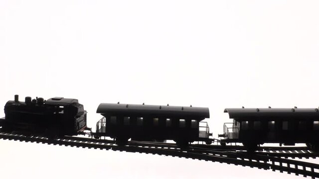 A locomotive with wagons moves on rails. Vintage model of electric toy steam locomotive with carriages, isolated against backlight background.
Western decoration background.