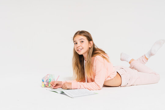 Cute smiling teen girl with long hair in pink hoodie doing homework isolated on the white background