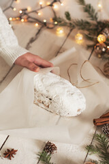 The hands of a cute girl wrap a Christmas Stollen in paper. Christmas stollen on wooden background. Traditional Christmas festive pastry dessert.