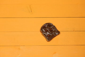 Slice of bread with spread chocolate cream and hazelnuts on yellow table. Serving a delicious breakfast concept.