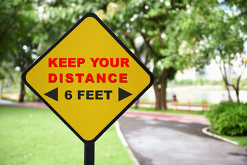 Keep your distance and 6 feet word on yellow sign at park background. Coronavirus disease 2019 or Covid-19 protect yourself concept and natural background idea