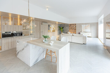 trendy modern interior design of a large studio in white and beige colors with large floor-to-ceiling windows. area of ​​white kitchen with an island and a recreation area