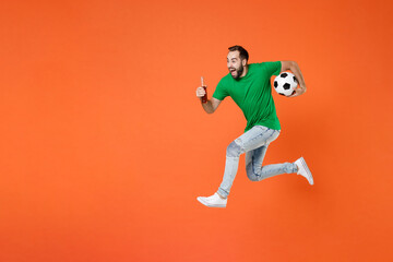 Fototapeta na wymiar Full length portrait screaming man football fan in green t-shirt cheer up support favorite team with soccer ball hold beer bottle jumping isolated on orange background. People sport leisure concept.