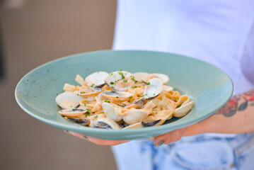 Photo of delicious pasta with clams. Waiter serving a meal in a restaurant. Eating out in restaurant.