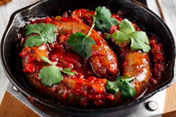 Large sausage in tomato sauce in cast iron pan