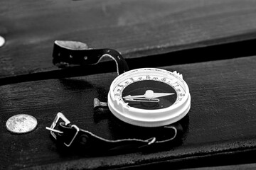 Black and white. Old tourist compass with a leather strap on a wooden board.