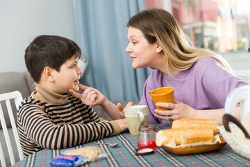 Portrait of young mother and son with tea talking at table indoors