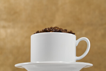 International day of coffee concept. close-up white coffee cup full of coffee beans on beige background.