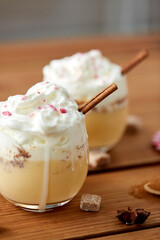 christmas and seasonal drinks concept - glasses of eggnog with whipped cream topping and cinnamon on wooden table