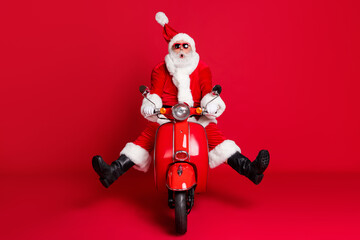 Full length photo of retired grandfather white beard crazy ride retro scooter wind blow face surprise avoid accident wear x-mas costume coat sunglass cap boots isolated red color background