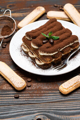 Classic tiramisu dessert on ceramic plate and savoiardi cookies on wooden background